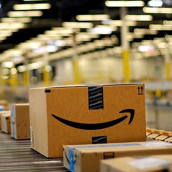A close-up of Amazon-branded cardboard boxes moving along a conveyor belt in a fulfillment center, representing an FBA prep center in Guangzhou.