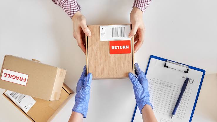 Hands in blue gloves and a plaid shirt inspecting a cardboard box with a "RETURN" label and barcode, next to a "FRAGILE" box and a checklist.