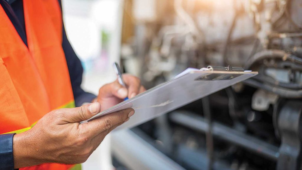 A worker in a high-visibility orange safety vest holding a clipboard and pen, inspecting a blurred industrial background, representing Amazon FBA returns management.